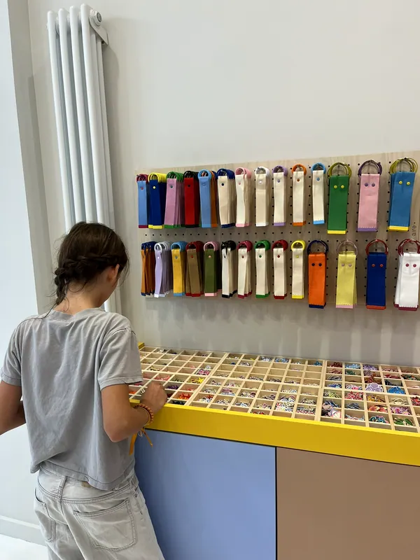 Une enfant fouille les boîtes d'écussons thermocollants rangées sur le comptoir jaune et violet de l'atelier
