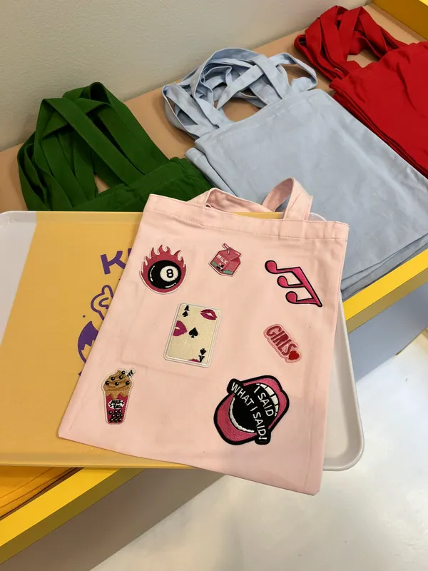 Deux tote bags personnalisés avec des écussons brodés, posés sur le comptoir de l'Atelier Kitsu