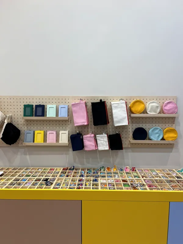 Le mur d'accessoires de l'Atelier Kitsu : tote bags, pochettes et porte-clés de toutes les couleurs, au-dessus des boîtes d'écussons