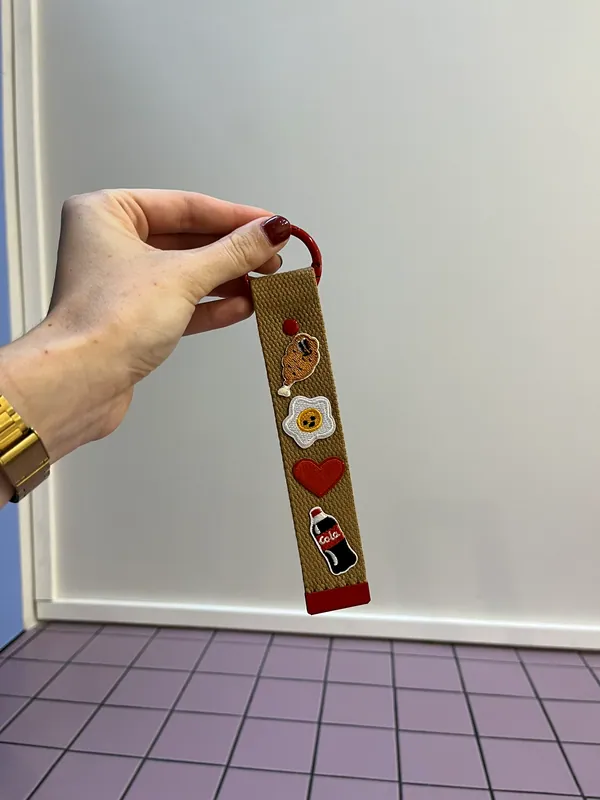 Porte-clés kaki personnalisé tenu à la main devant le mur de la boutique
