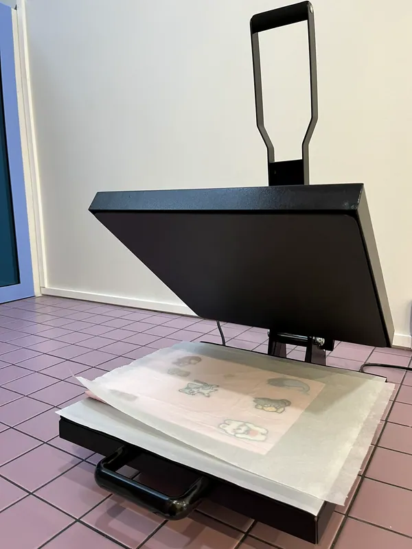 La presse à chaud de l'atelier, ouverte sur un tote bag couvert d'écussons prêt à être thermocollé
